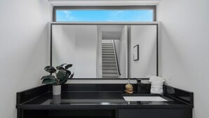 Une salle de bain moderne avec un meuble-lavabo noir, une plante en pot, un miroir et une vue sur un escalier.