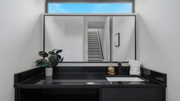 Um banheiro moderno com toucador preto, uma planta em vaso, um espelho e vista para uma escada.