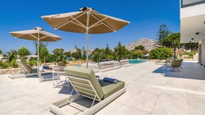 Un espace aménagé au bord de la piscine, avec des chaises longues et des parasols, une piscine, et un paysage montagneux en arrière-plan.