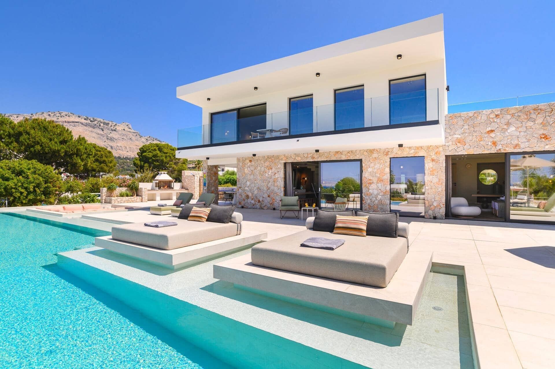 Une maison moderne à deux étages, dotée d’une piscine, d’un espace salon extérieur et d’une façade en pierre.