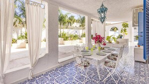 A sunlit patio with a table set for dining, surrounded by white columns and blue patterned flooring. - Villa Blu Marino by Villa Plus (Syracuse)