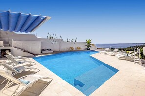 A pool with clear blue water, surrounded by lounge chairs and a view of the sea. - Villa Blu Marino by Villa Plus (Syracuse)