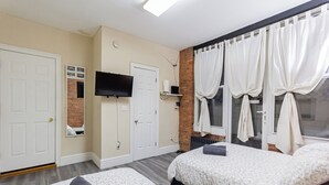Habitación de hotel con dos camas, televisión de pantalla plana, una pared de ladrillo decorativa y una ventana con cortinas.