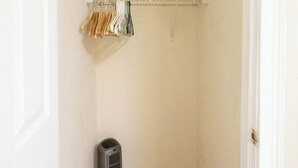 Una habitación pequeña y estrecha con suelo de madera, una puerta blanca, un armario con ropa colgada y un radiador.