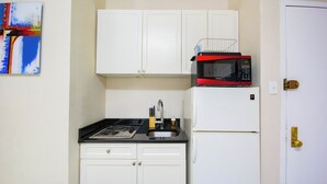 Una cocina compacta con armarios blancos, una encimera negra, un microondas rojo y negro, una estufa y un refrigerador.