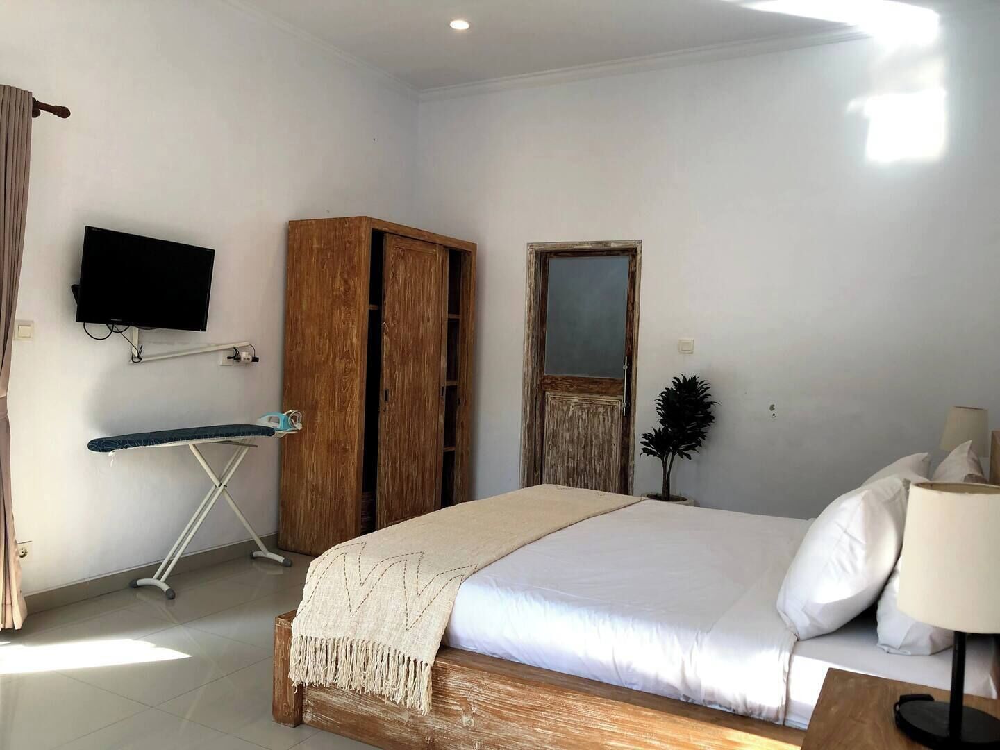 A bedroom with a bed, a TV mounted on the wall, a wooden wardrobe, and a small plant.