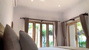 Quarto com cama, cortinas e vista para o verde lá fora.