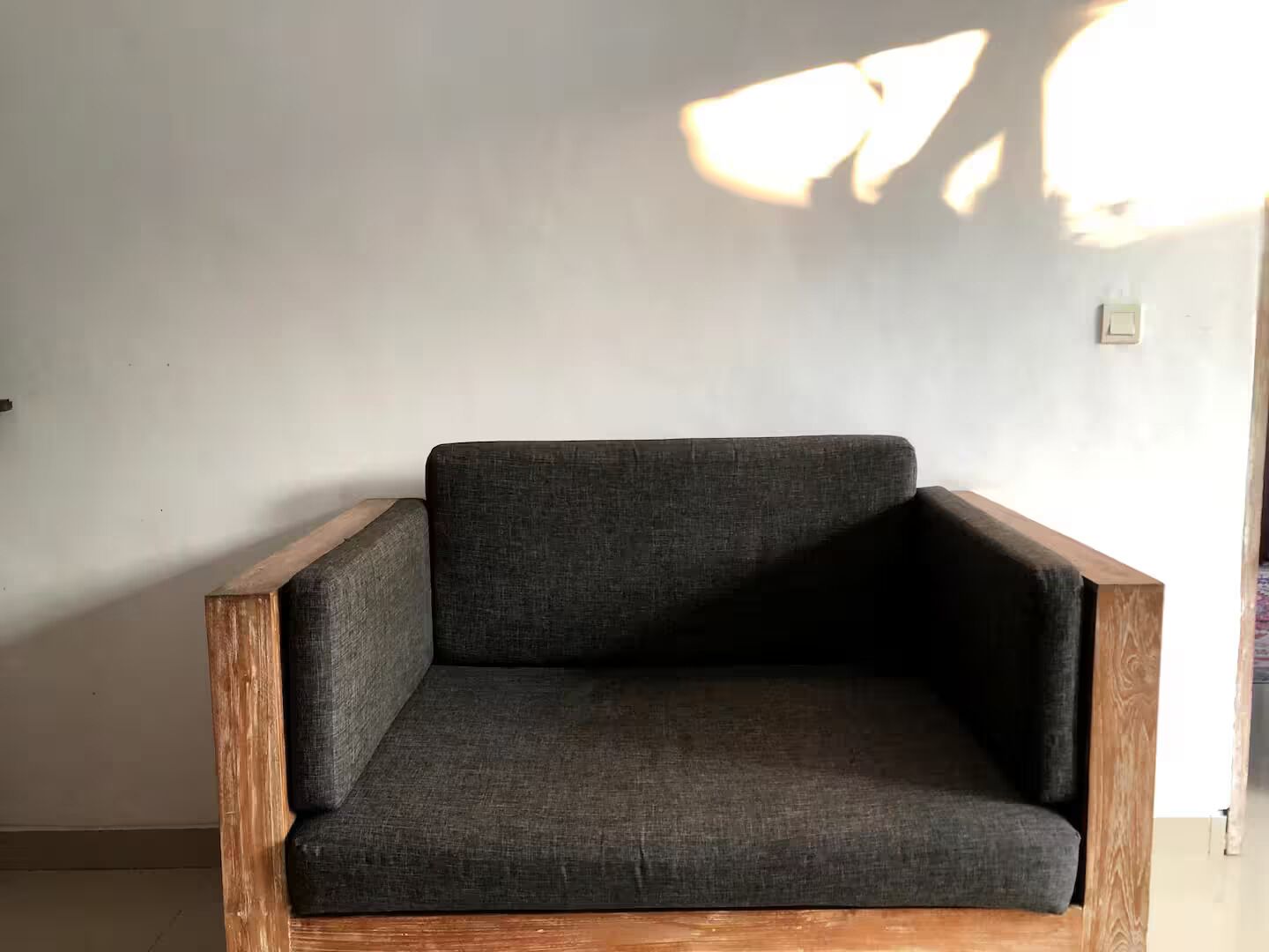 A dark grey upholstered armchair with wooden armrests and legs, positioned against a plain wall.