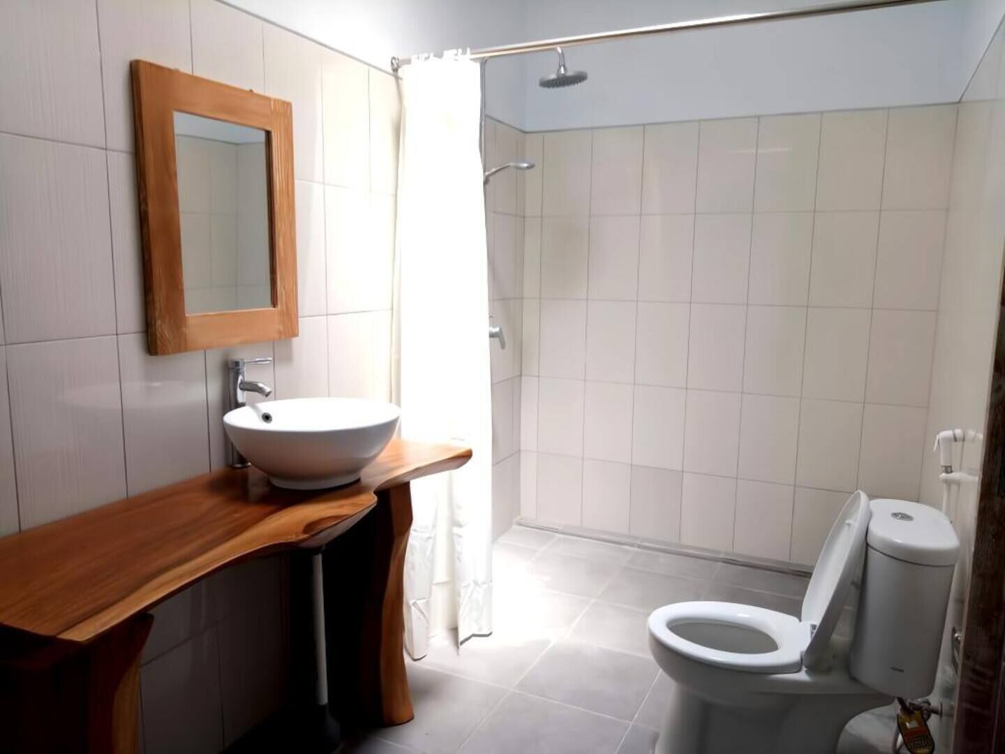 Un baño con tocador de madera, lavamanos blanco, inodoro y zona de ducha.