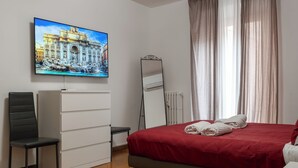 A hotel room with a bed, a TV mounted on the wall, a chair, a dresser, and a window with curtains. - Trevi Ducal Palace I (Roma)