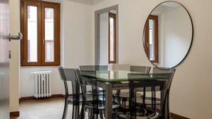 A dining area with a glass table and chairs, a round mirror on the wall, and windows with wooden frames. - Trevi Ducal Palace I (Roma)
