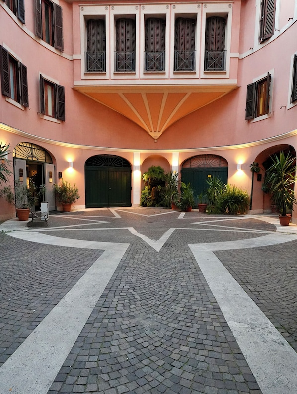 Un patio con un espacio central abierto, plantas en macetas y un edificio con varias ventanas y una puerta verde.