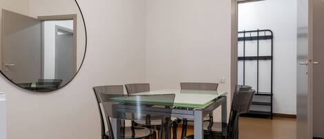 A dining area with a glass table and chairs, a round mirror, and a door leading to another room.