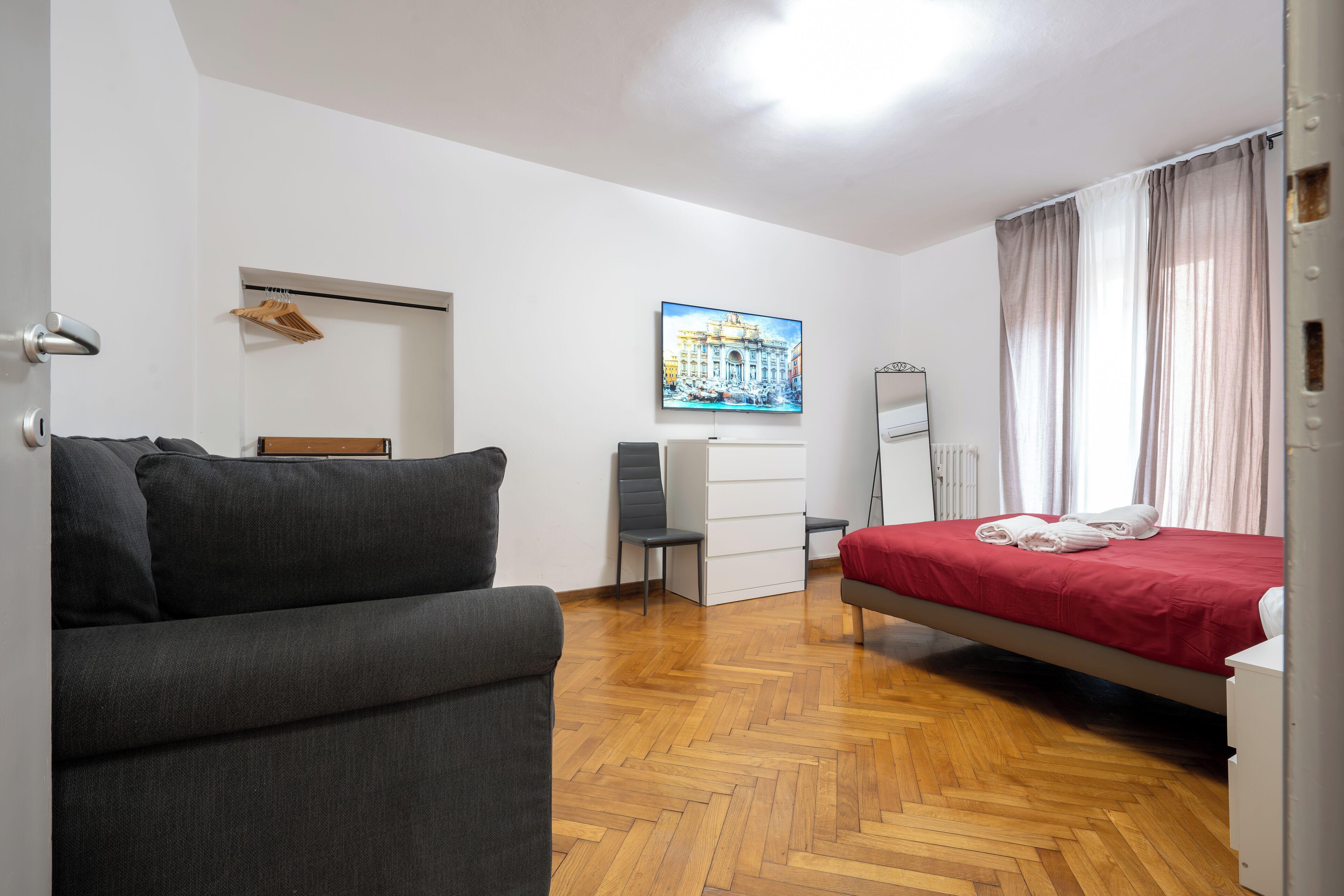 A bedroom with a bed, a sofa, a desk, a chair, a radiator, and a painting on the wall.