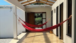 A covered corridor with a wooden floor, a hammock, and a view of greenery through a door. - Beautiful country house in San Martin (pet and family friendly) (San Martín)