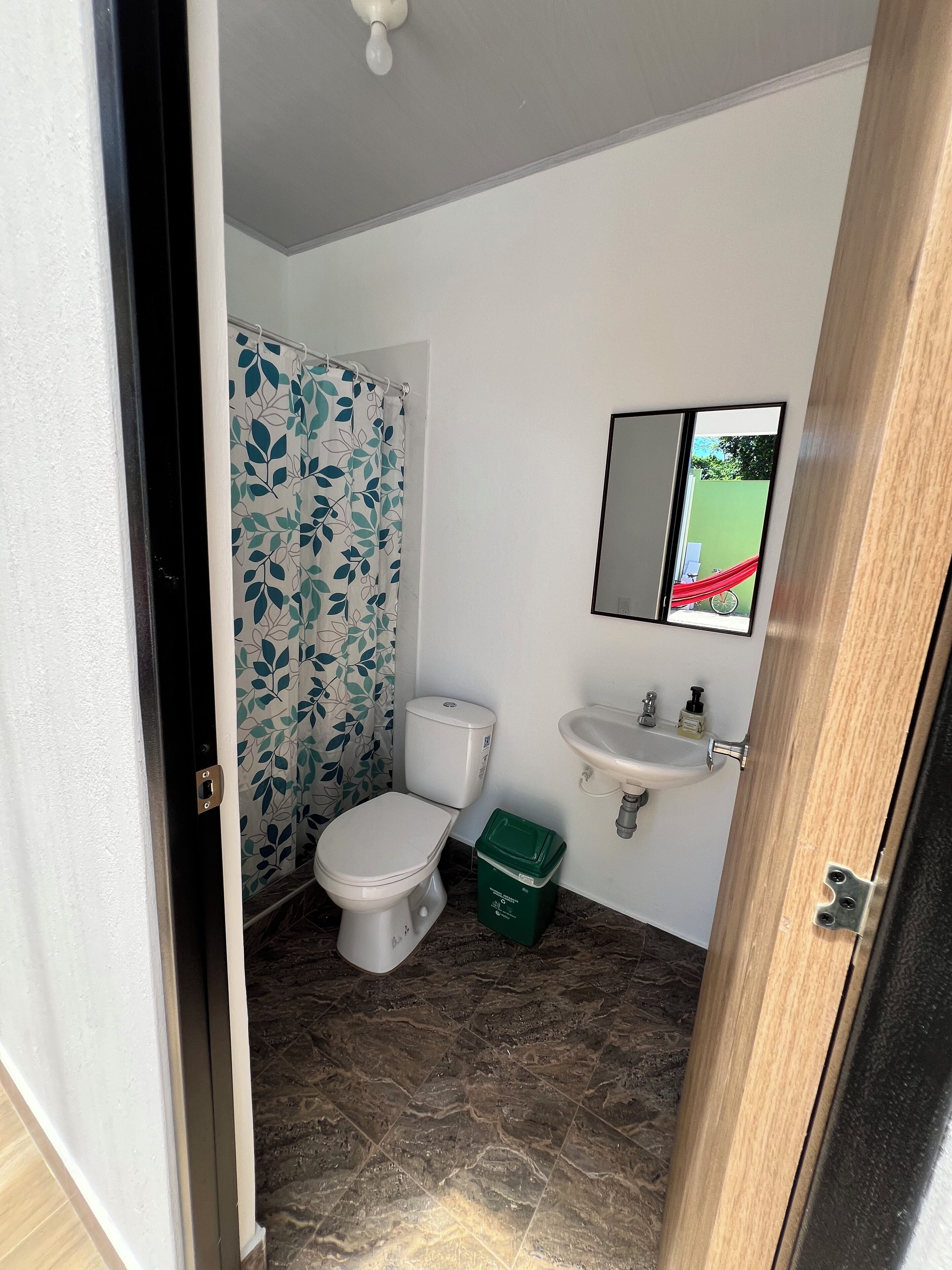 Une salle de bain avec des toilettes, une poubelle verte, un lavabo et un miroir.