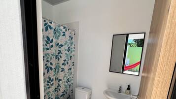 Une salle de bain avec des toilettes, une poubelle verte, un lavabo et un miroir.