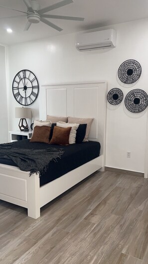 Una camera da letto moderna con un letto bianco, una ventola a soffitto, un condizionatore d'aria e decorazioni a parete.