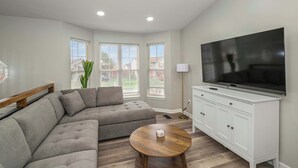 A modern living room with a sectional sofa, a round coffee table, a TV, and a white cabinet. - The Restful Ark (Crittenden)