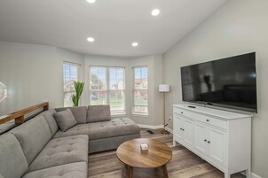 Una sala de estar moderna con un sofá seccional, una mesa redonda de centro, un televisor y un mueble blanco.