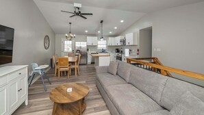 A modern living room with a sofa, dining table, and chairs. There is a kitchen area with cabinets and appliances in the background. - The Restful Ark (Crittenden)