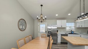 A modern kitchen with a dining area, featuring a chandelier, stainless steel appliances, and a wooden dining table. - The Restful Ark (Crittenden)