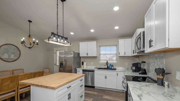 A modern kitchen with white cabinets, a wooden island, stainless steel appliances, and a chandelier. - The Restful Ark (Crittenden)