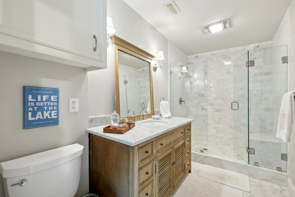 Un baño moderno con tocador de mármol, cabina de ducha de vidrio y un letrero motivacional en la pared.