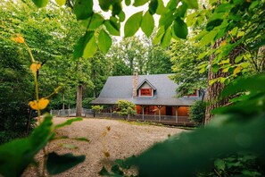 A cabin with a stone chimney, surrounded by dense forest.