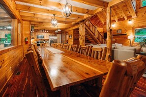 Eine Holzhütte mit einem langen Esstisch, Stühlen, einer Küchenzeile und einer Treppe.