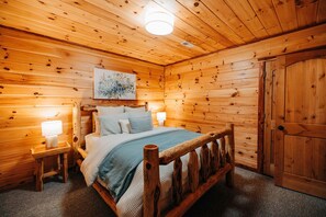 Ein Schlafzimmer in einer Holzhütte, mit einem Bett, Nachttischlampen, einem Bild und einem Kleiderschrank.