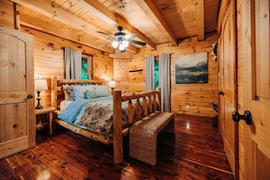 A wooden cabin bedroom with a bed, a ceiling fan, a bench, and a painting on the wall. - Rustic Cedar Inn | Luxury 6BR Lodge, Kids Loft (Rockbridge)