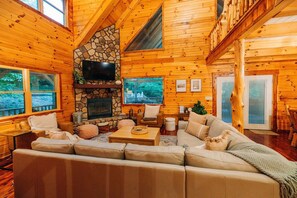 A log cabin interior with a stone fireplace, wooden walls, a sofa, and a television.