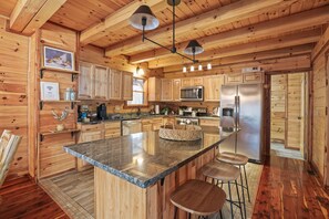 A wooden cabin kitchen with granite countertops, a central island, bar stools, and modern appliances.