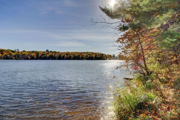 Ein ruhiger See mit klarem Wasser, das den Himmel spiegelt, umgeben von Bäumen im Herbstlaub.