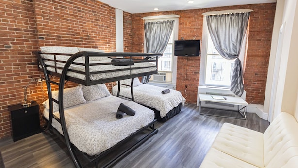 A room with bunk beds, a flat-screen TV, a window with curtains, and a sofa.