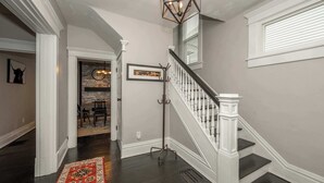Un escalier avec des balustrades blanches et des marches sombres, menant à un palier sur lequel se trouve un tapis rouge à motifs.