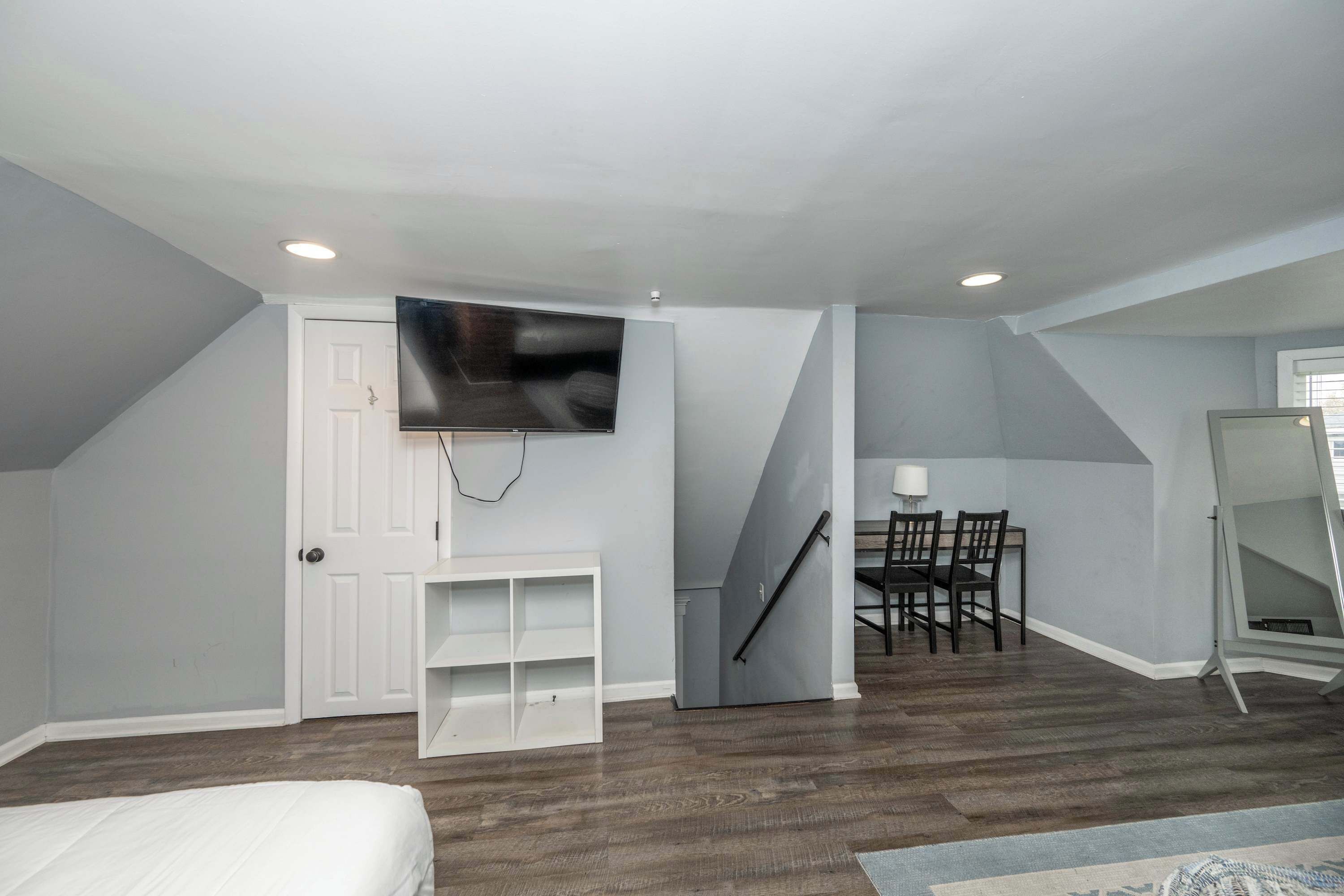 A room with a bed, a TV mounted on the wall, a desk with a chair, and a staircase.