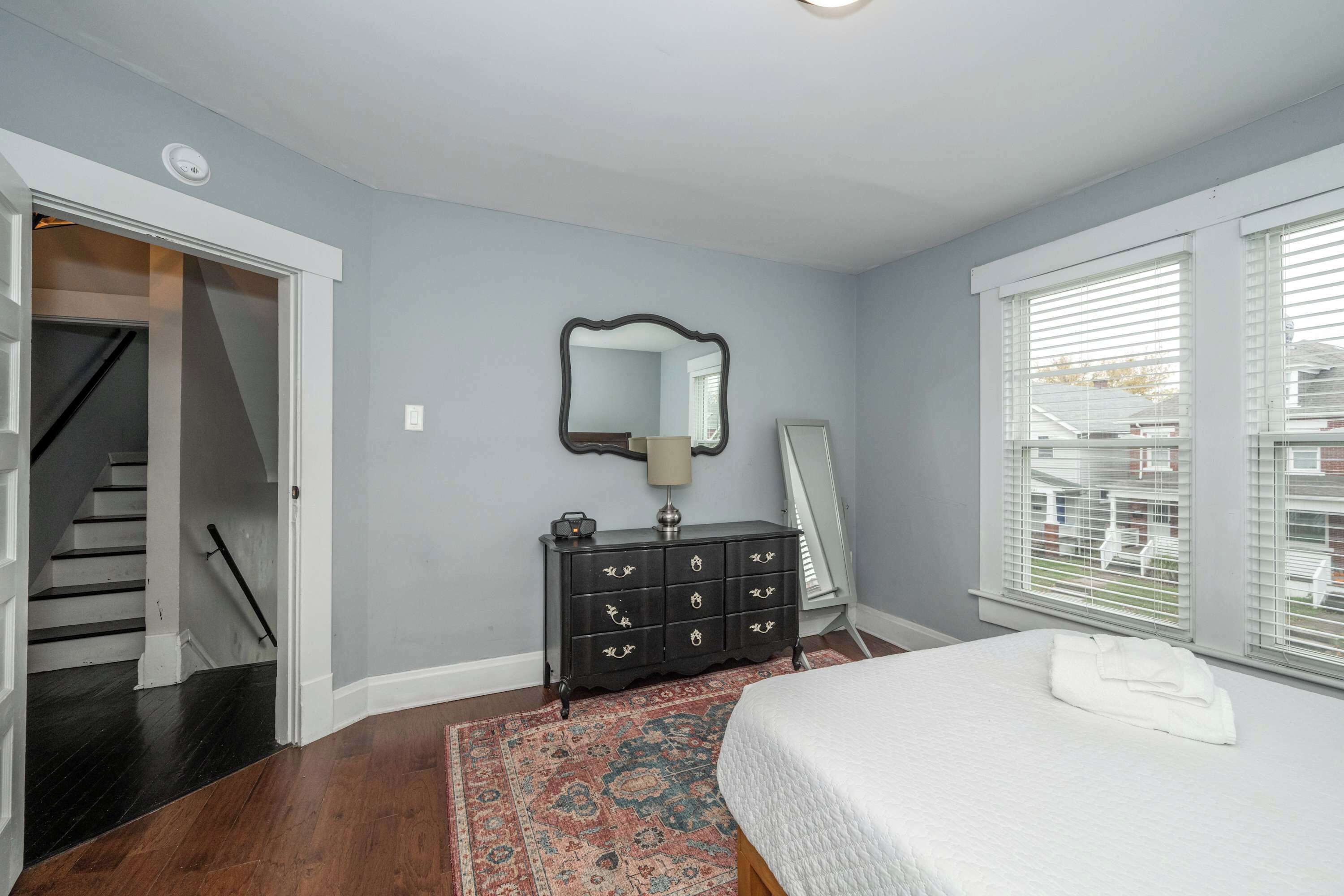 A bedroom with a bed, dresser, mirror, and a view of the outside through a window.