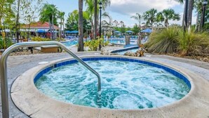 Un bain à remous entouré de palmiers et un espace piscine avec des chaises longues.