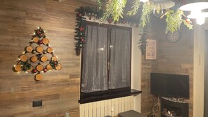 A cozy living room with a wooden floor, a fireplace, a TV, and a Christmas tree decoration.