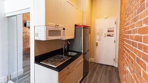 A compact kitchen with a microwave, stove, and refrigerator, a door with a notice, and a brick wall. - Chic STUDIO with WiFi near Empire State Building (New York)