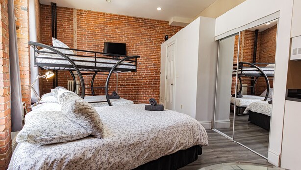 A bedroom with a brick wall, a bunk bed, a flat-screen TV, and a large mirror. - Chic STUDIO with WiFi near Empire State Building (New York)