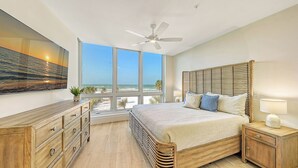 Een slaapkamer met een groot bed, een houten hoofdbord en uitzicht op de oceaan door grote ramen.