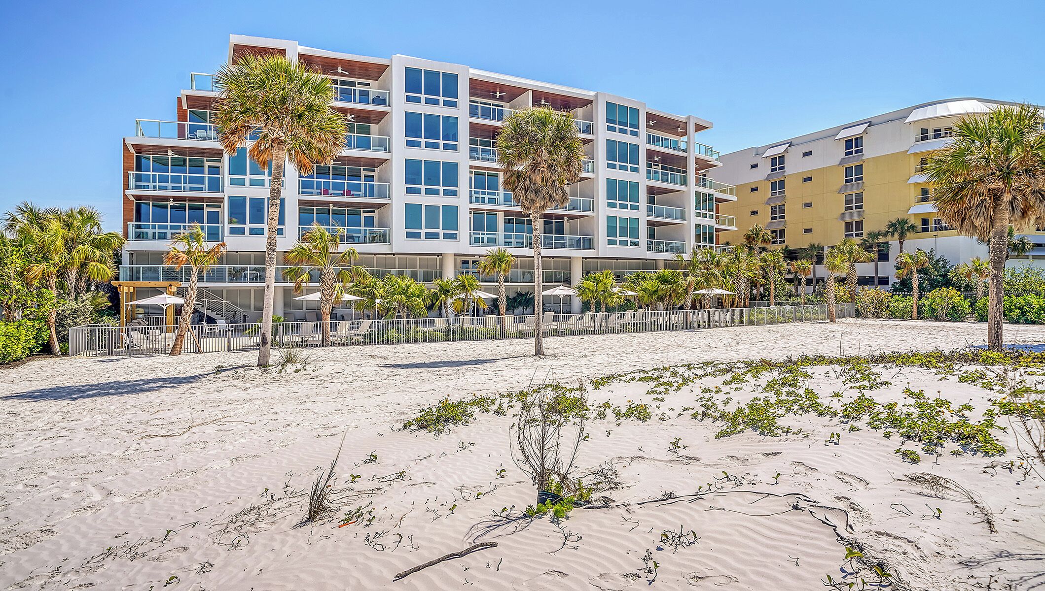 A beachfront hotel with multiple floors, outdoor seating, and palm trees.