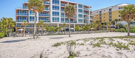 A beachfront hotel with multiple floors, outdoor seating, and palm trees.