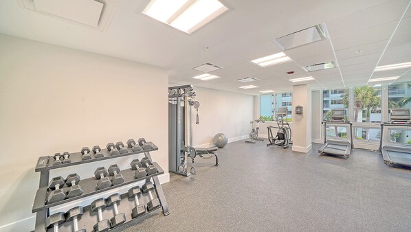 Une salle de sport équipée de matériel d’exercice, notamment des haltères, un vélo d’appartement et un tapis de course.