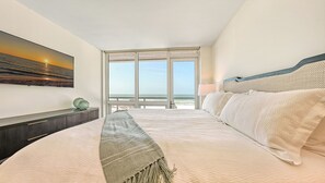 A bedroom with a large bed, a view of the ocean, a painting on the wall, and a lamp. - Beathtaking Costal Luxury with Direct Beach and Gulf Views: Residence 405 (Siesta Key)