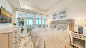 Un dormitorio moderno con una cama grande, un escritorio y vistas al océano a través de puertas correderas de vidrio.