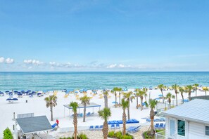 A beach resort with white sand, palm trees, and blue umbrellas.